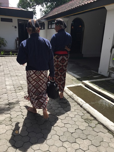 Two men in traditional Indonesian clothes walking together through a courtyard