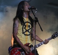 Singer of Indonesian indie band in power stance with electric guitar, singing into microphone in front of a haze of smoke.