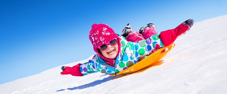 Child sliding down a snow slope on a saucer disc sled.