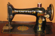 A black metal sewing machine with brown cotton on the spindle. The machine is decorated with a red and gold design