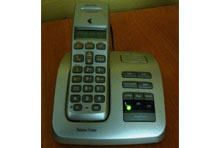 A white cordless phone on a charger base. The phone has push button numbers