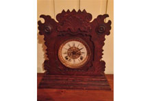 A brown wooden carved clock that has a white face with Roman numerals
