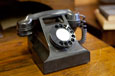 A black phone with a dial at the front and a hand piece and cord at the top.