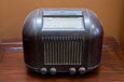 A small shiny brown radio with four dials and a tuning window on the top and a speaker at the front