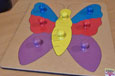 A wooden puzzle of a butterfly with 2 yellow pieces for the body and a blue, red and purple piece for each wing.