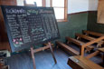 An 1880s classroom containing a blackboard standing on an easel and covered with decorative text and multiplication tables.