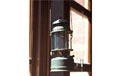 A lantern, with a metal top and bottom and glass in the middle, attached to a wall.