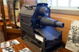 A black metal epidiascope with a long lens on a table.