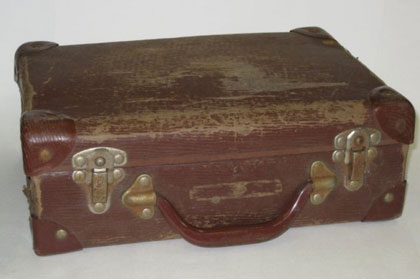 A worn, scratched brown case with metal clips and brown curved handle.