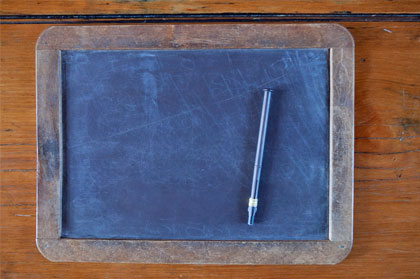 A rectangular slate board in a wooden frame with a slate pencil placed on the board.