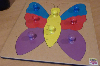 A wooden puzzle of a butterfly with 2 yellow pieces for the body and a blue, red and purple piece for each wing.