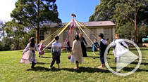 Children in school playground holding coloured ribbons preparing to skip around the maypole