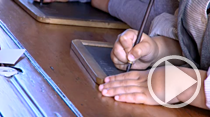 The hands of a child using a slate pencil to write on a slate board