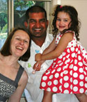 A young girl has her photo taken with her parents; her dad is holding her and she is wearing a dress with red and white dots