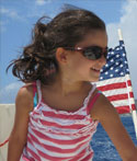 A girl wears sunglasses on a boat out on the water; an American flag flies behind her