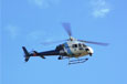 A blue and white helicopter with three blades flying in a clear blue sky.