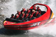A large red jet boat moving on the water with 14 people inside.