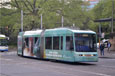 A light blue tram, with a large window at the front and smaller windows on the side, rounding a bend.