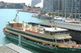 A ferry with a green hull and a cream body and many people on board at Circular Quay.