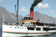 An old white steam ship with a red and black funnel; black smoke is pouring out of the funnel.