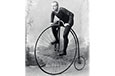 A penny farthing bicycle with a very large front wheel and a small back wheel; the handlebars are above the large wheel.
