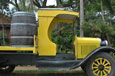 A vintage yellow sideless truck with a barrel on the tray.