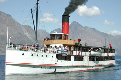 An old white steam ship with a red and black funnel. Black smoke is pouring out of the funnel