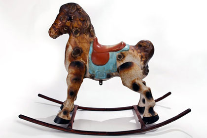 An old spotted rusty rocking horse made of metal with a blue blanket and a red saddle.