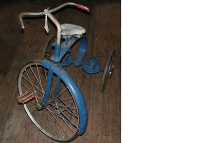 A rusty blue metal tricycle with white seat and red hand grip