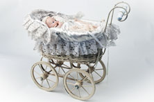 A doll's pram with four large wheels and a lace cover. A doll is lying in the pram.