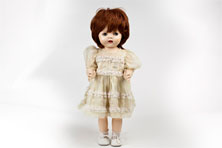 A female toddler doll made from hard plastic. She has blue eyes and auburn hair