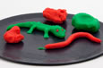 Three pieces of play-doh and a play-doh green lizard and red snake displayed on a flat black plate.