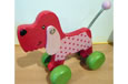 A smiling pink pull along dog with pink spotty sides and four green wheels.