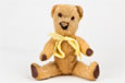 An old teddy bear with orange fur, brown glass eyes, four paws and a yellow ribbon.