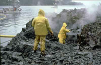 two people wearing protective clothing pressure blasing black rocks that are coated in oil