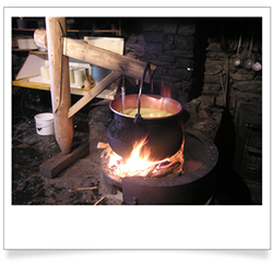 Ac opper vat containing milk suspended over an open fire.