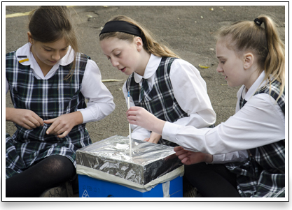 students measuring temperature from a reflective roof model