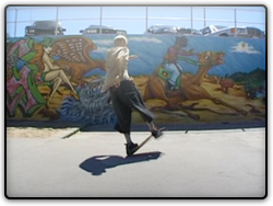 A man, with his back to the camera, is suspended mid movement on his skateboard, in front of a colourful wall mural