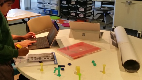Student designing on a computer surrounded by 3D printed objects on a table