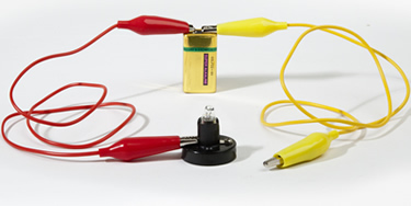 Photograph of a circuit showing a wire connected from a battery to a lamp and another wire from the other side of the lamp back to the other side of the battery. One of the wires is disconnected.