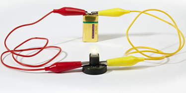 Photograph of a circuit showing a wire connected from a battery to a lamp and another wire from the other side of the lamp back to the other side of the battery.