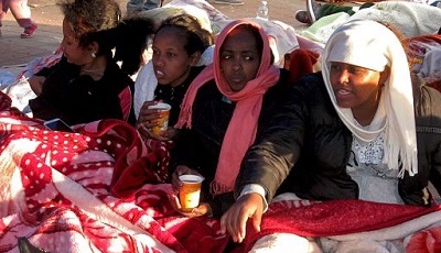 Photo of four female African refugees sitting on the ground. They look cold.