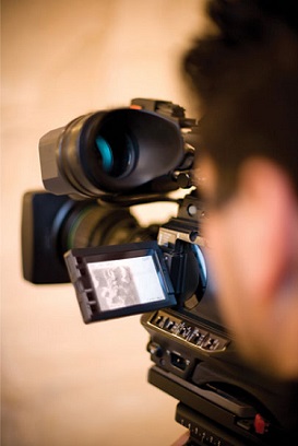 Photo of man using a video camera looking from behind into the camera