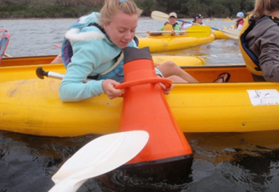 Students in canoes use equipment to look at the contents of the water.