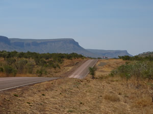 An empty road disappears over a low hill with rugged escarpment in the background