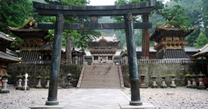 Japanese Torii gate in front of steps leading to three buildings.