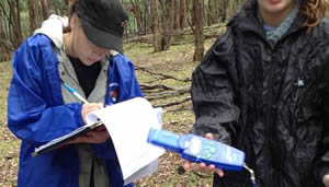 Students on a field trip, one is writing in a notebook and another is holding equipment