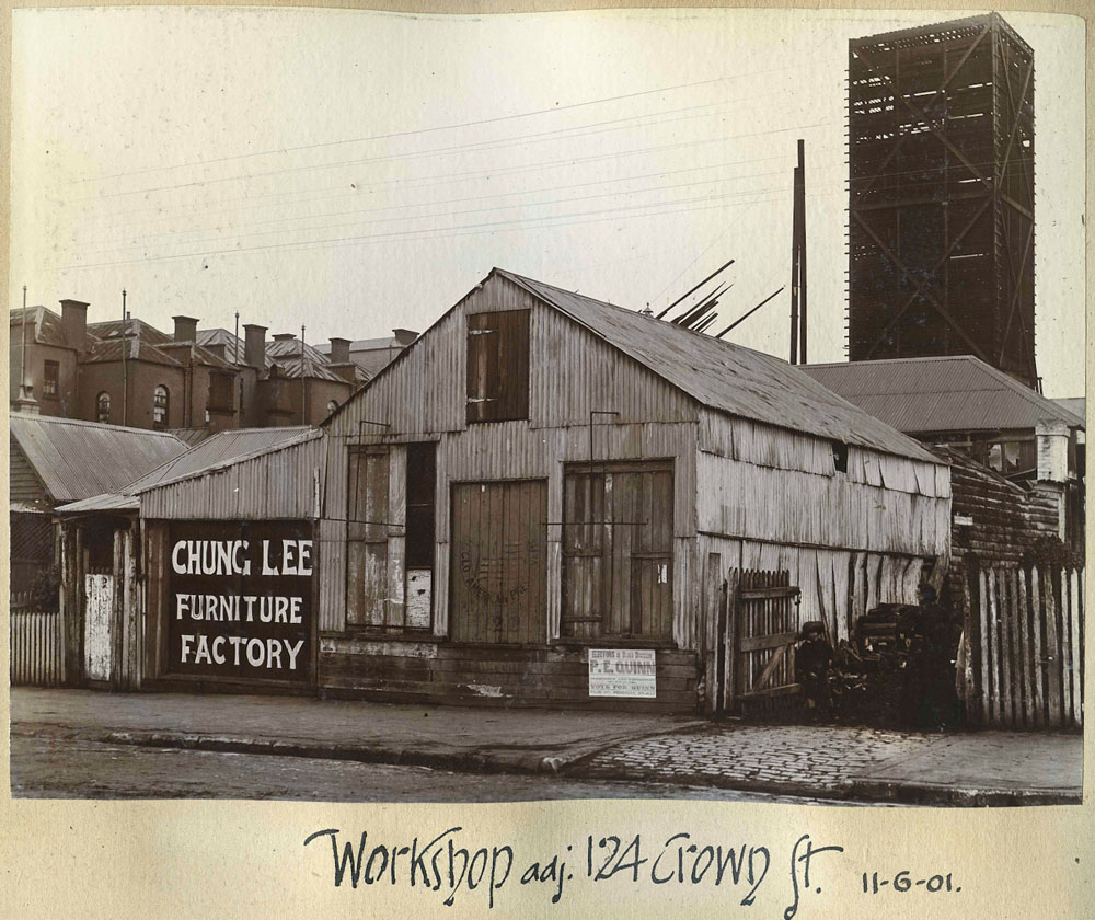 Black and white photo showing the outside of the Chung Lee furniture factory. Working class residential buildings are in the background