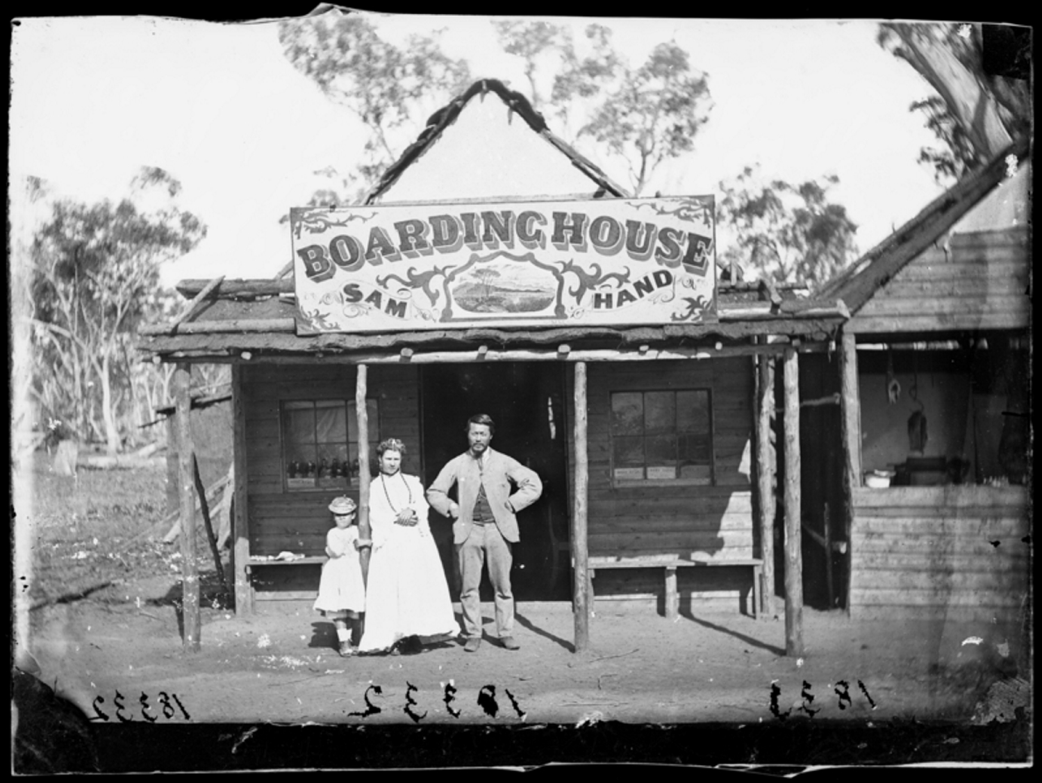 Photo of old boarding house belonging to Sam Hand. Standing in front of the boarding house is Sam Hand, his wife and daughter.