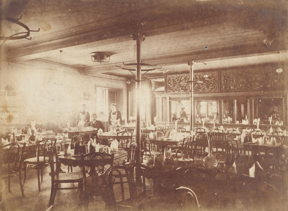 Photograph showing Quong Tart and two waitresses in one of Quong Tart's tea rooms. In picture at several tables and chairs.
